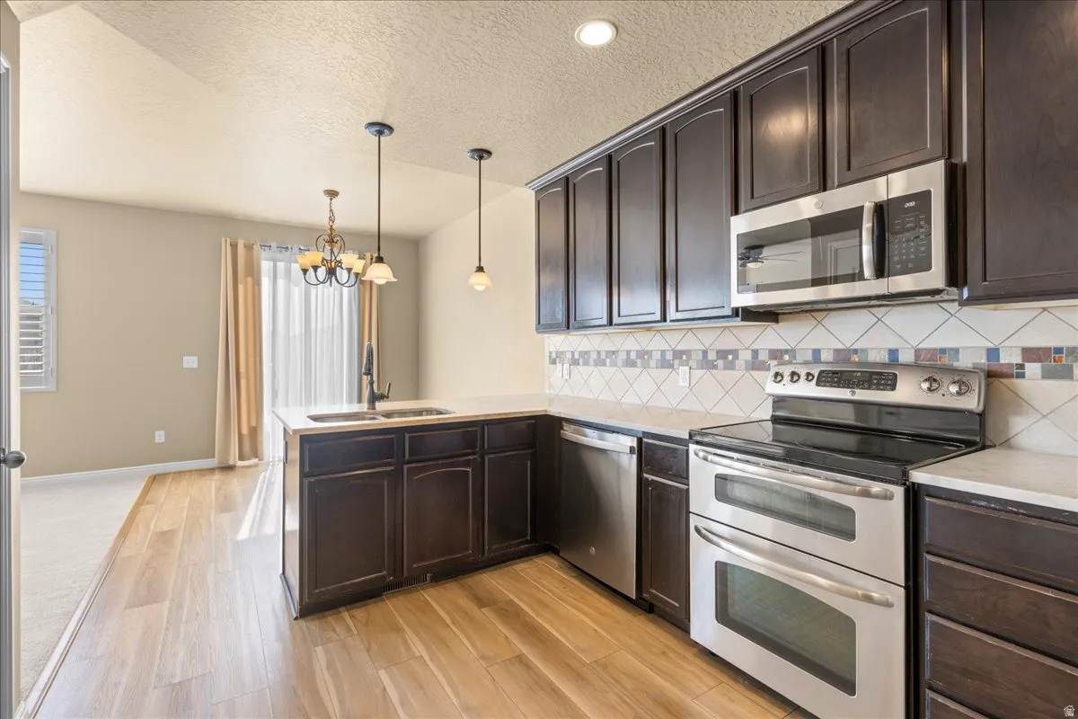 Kitchen featuring dark wood finish cabinets, stainless steel appliances, backsplash, a peninsula, and a textured ceiling