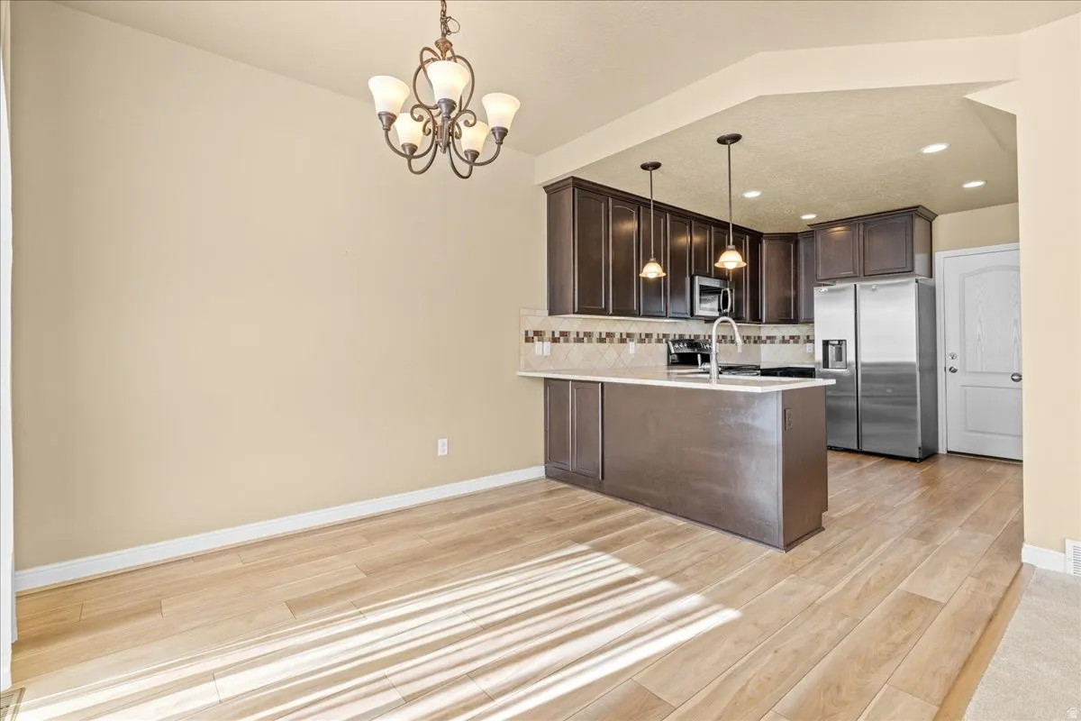 Kitchen with dark wood finish cabinets, stainless steel appliances, a peninsula, light wood-style floors, and suspended lighting