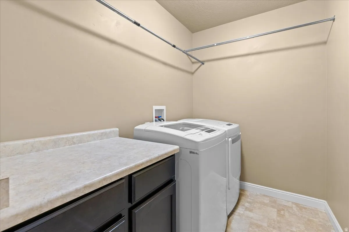 Laundry room with independent washer and dryer, a textured ceiling, and stone finish floors