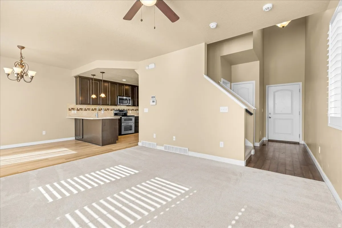 Unfurnished living room featuring light carpet, a ceiling fan, a chandelier, and light wood-style flooring