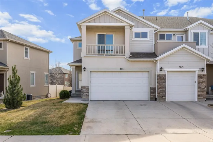 View of front of home featuring a balcony, stone siding, a front yard, and concrete driveway