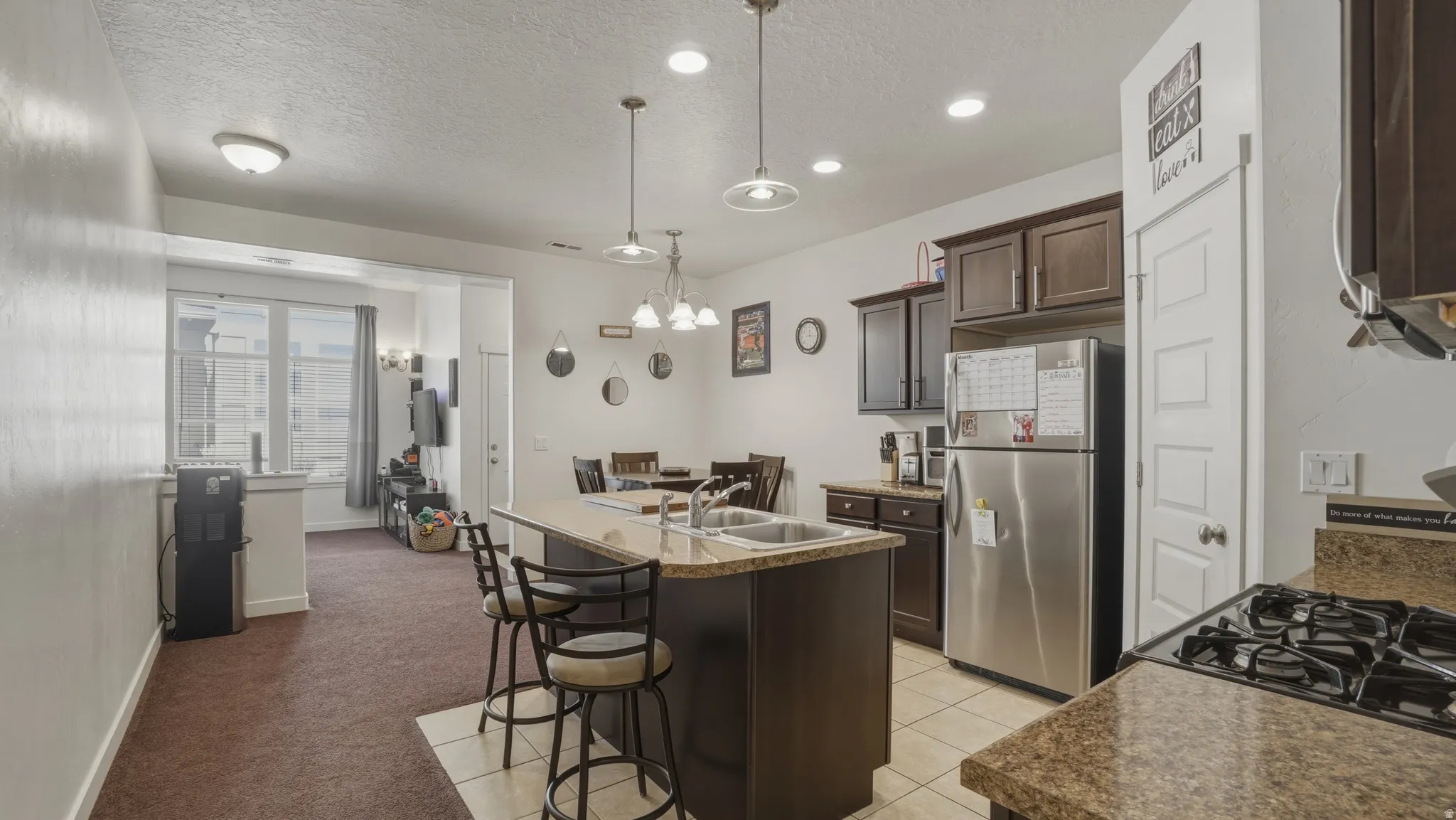 Kitchen with an island with sink, freestanding refrigerator, a kitchen breakfast bar, a textured ceiling, and dark wood finish cabinets