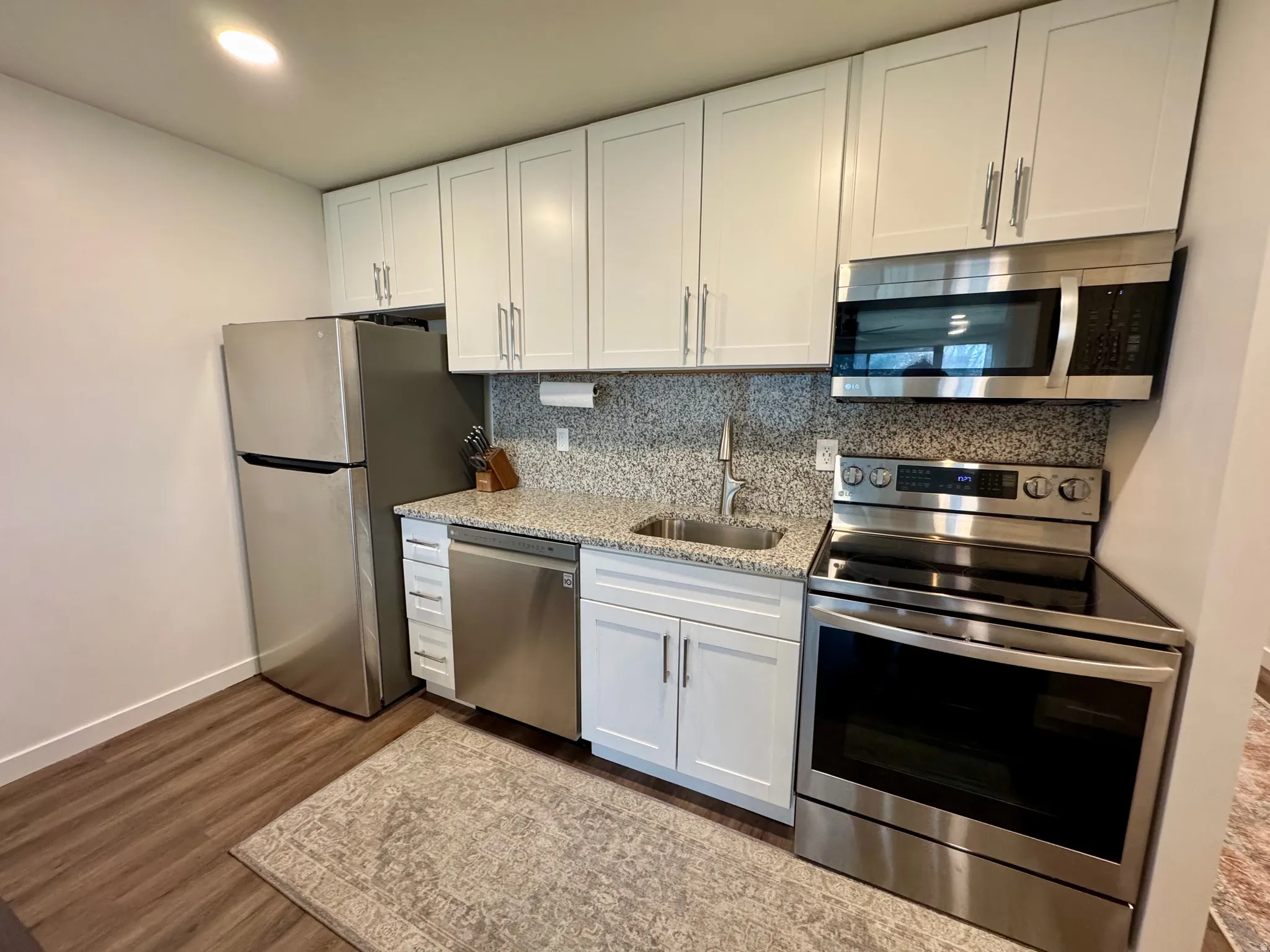 Kitchen with stainless steel appliances, white cabinets, light stone countertops, decorative backsplash, and recessed lighting