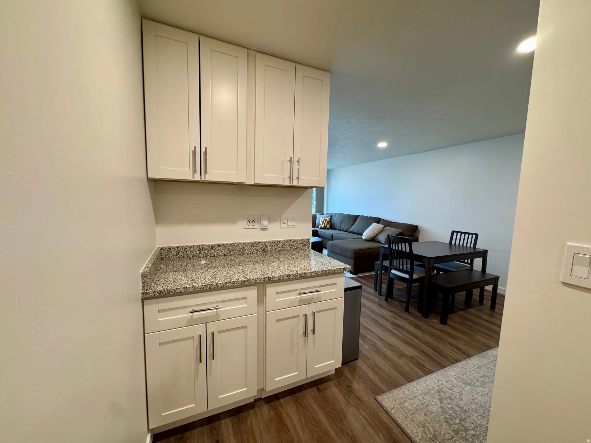 Kitchen with light stone counters, white cabinets, dark wood-type flooring, and recessed lighting