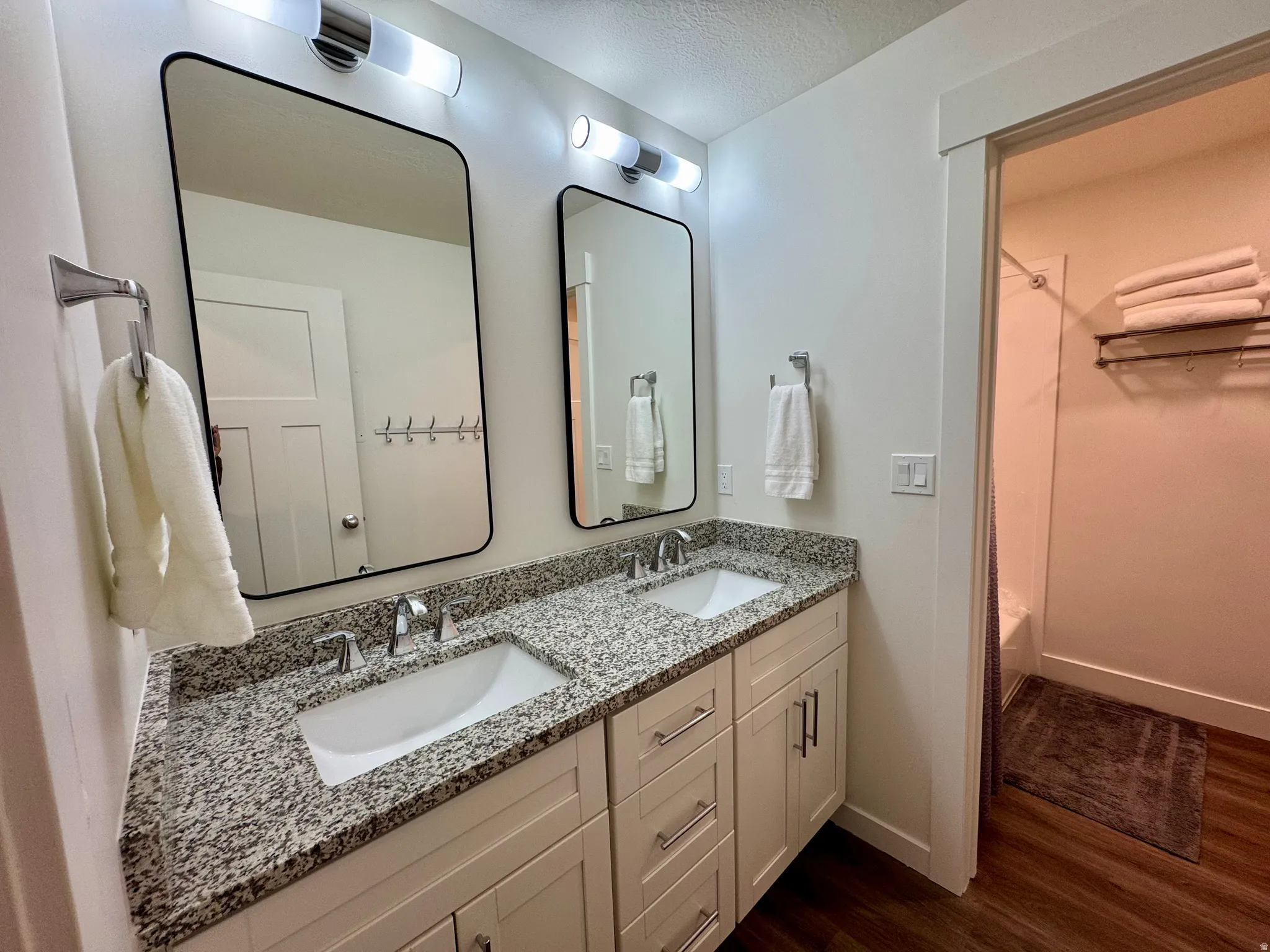 Full bathroom featuring double vanity, a textured ceiling, dark wood-style floors, and  shower combination