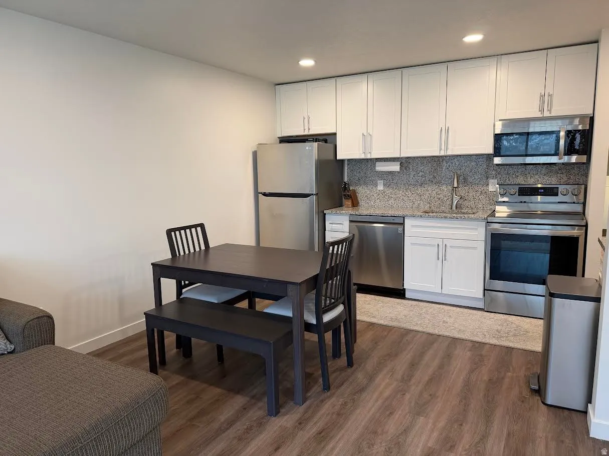 Kitchen with stainless steel appliances, white cabinetry, dark wood finished floors, light stone countertops, and recessed lighting