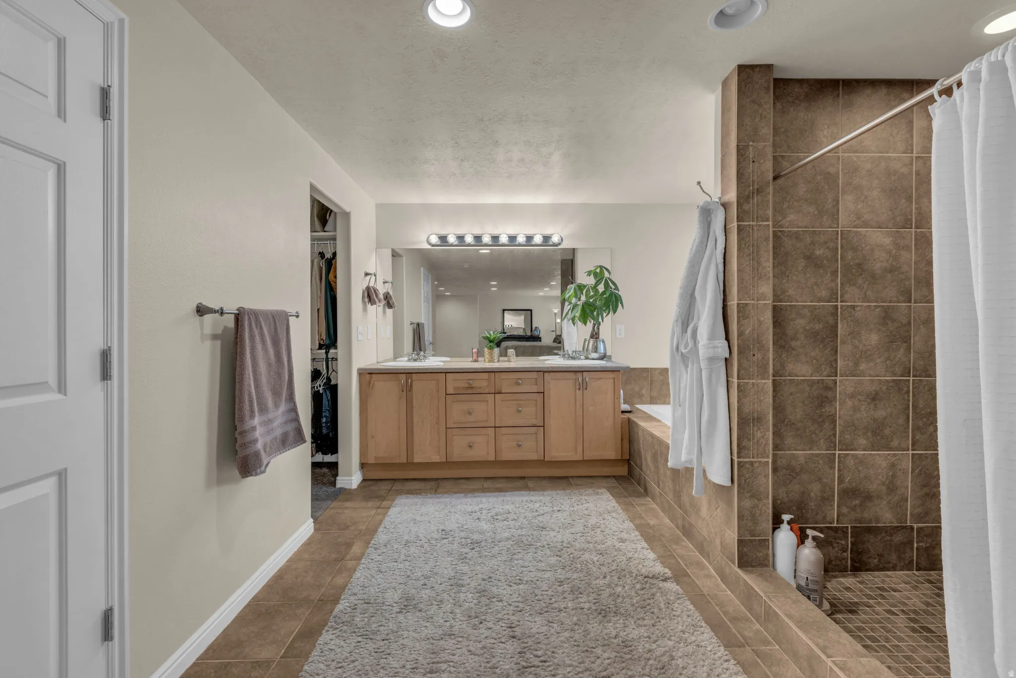 Bathroom with tiled shower, double vanity, a bath, dark tile patterned flooring, and a spacious closet