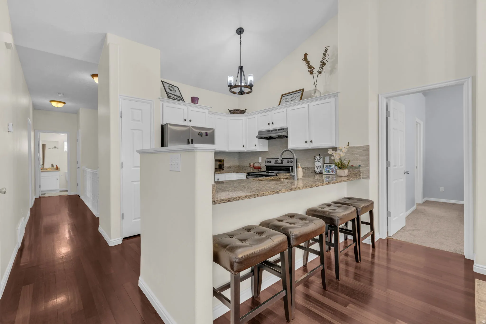 Kitchen with vaulted ceiling, dark wood-style flooring, light stone countertops, a kitchen breakfast bar, and a peninsula