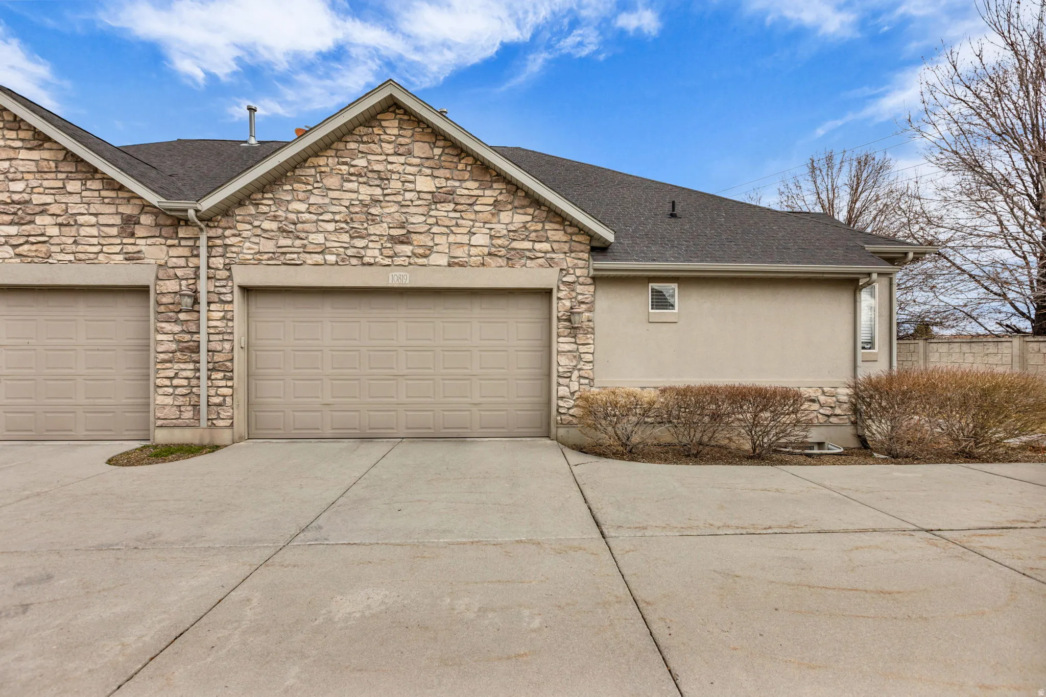 View of side of property featuring stone siding, concrete driveway, roof with shingles, and a garage
