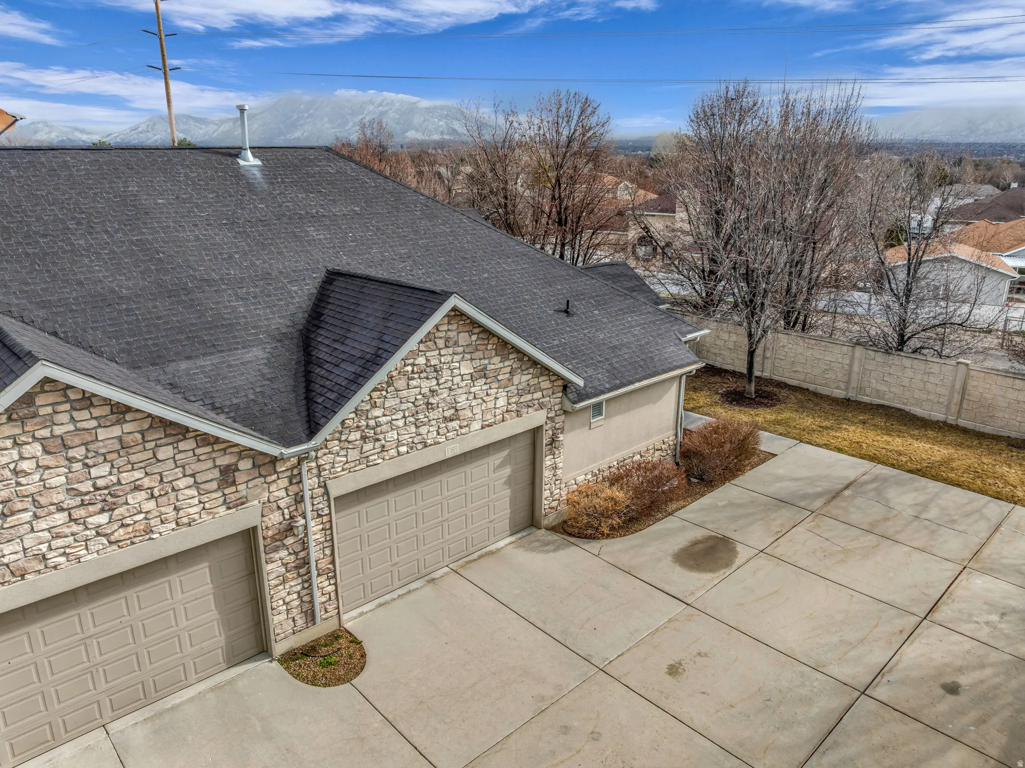 View of front of property featuring a shingled roof, stone siding, concrete driveway, and a garage