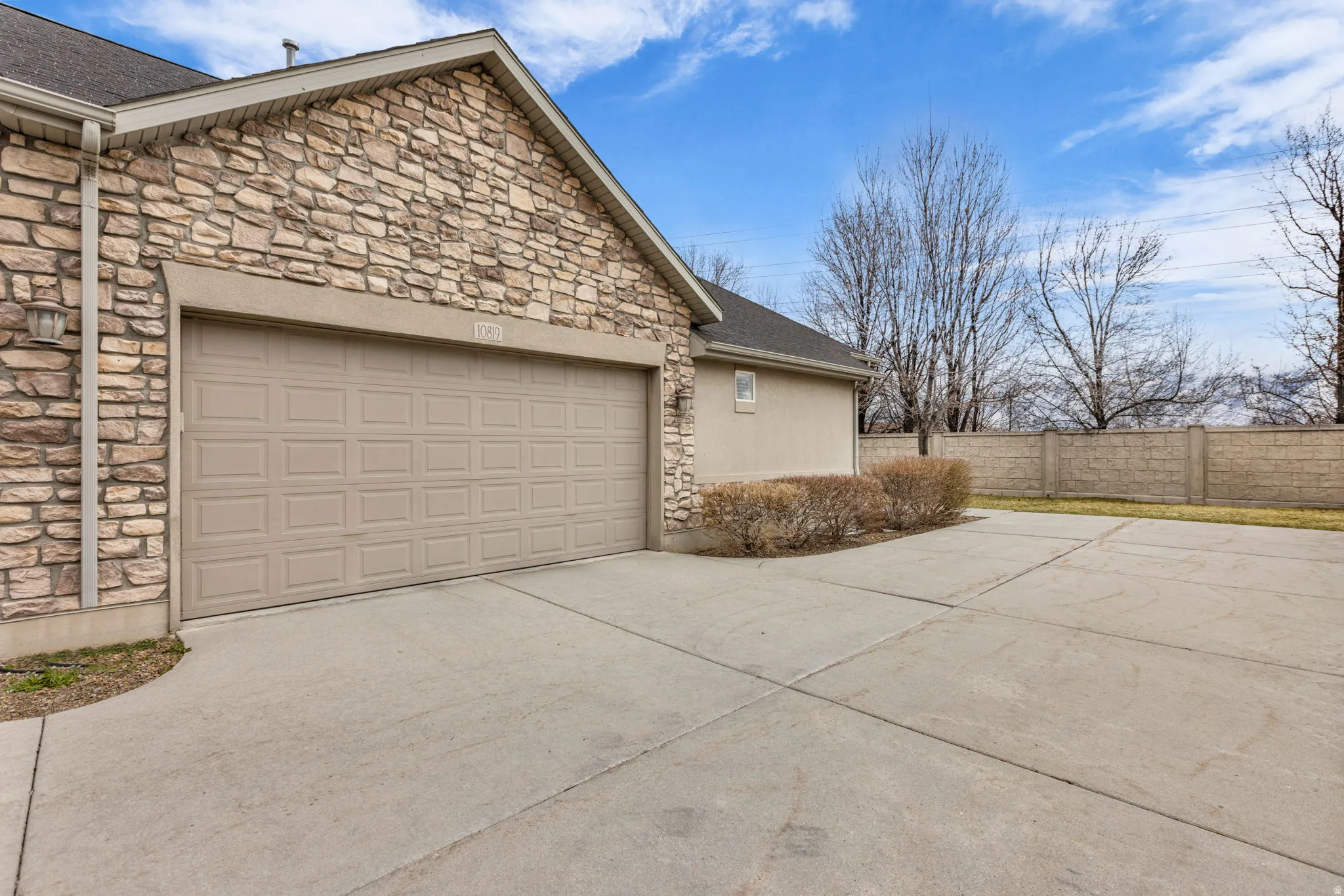 View of side of home featuring stone siding, a garage, driveway, and a shingled roof