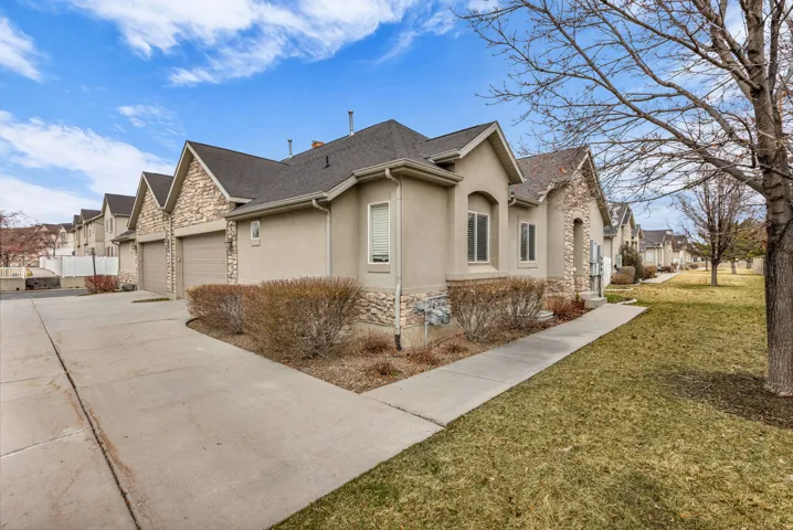 View of side of property with stone siding, stucco siding, a garage, concrete driveway, and a yard