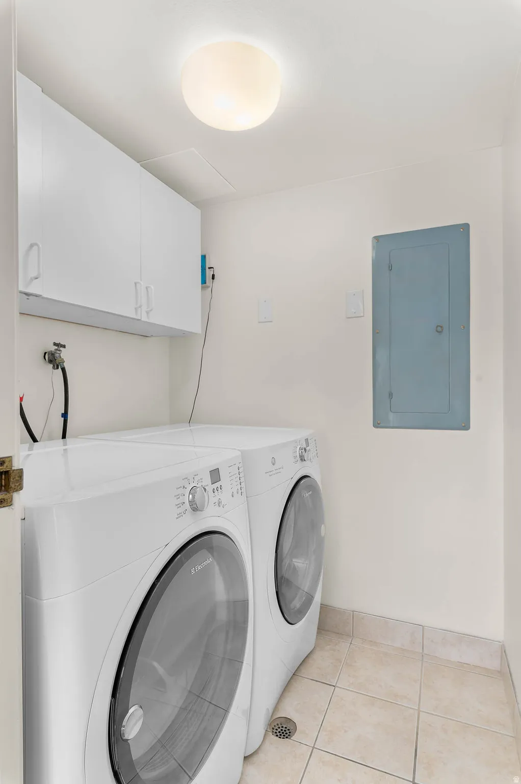 Laundry room with electric panel, washer and clothes dryer, cabinet space, and light tile patterned flooring
