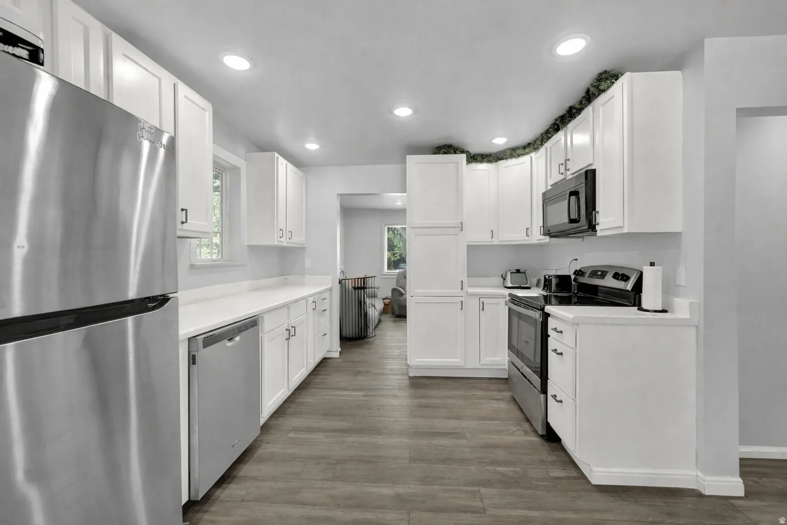 Kitchen with stainless steel appliances, white cabinets, light countertops, dark wood-style floors, and recessed lighting
