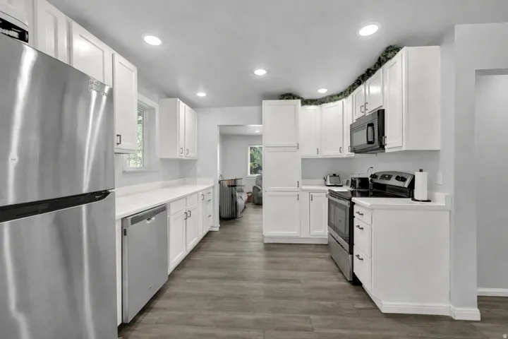 Kitchen with stainless steel appliances, white cabinets, light countertops, dark wood-style floors, and recessed lighting