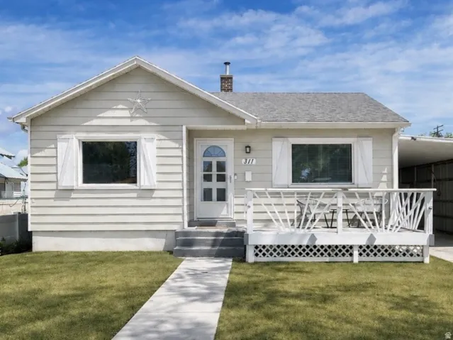 Exterior featuring horizontal siding, a covered front porch with decorative railing, an arched transom entry door, a paved driveway, and an attached carport