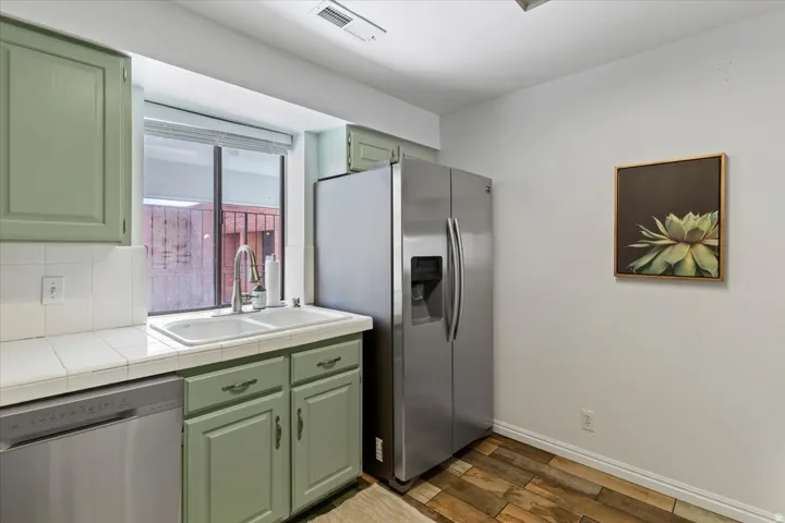 Kitchen featuring green cabinetry, stainless steel appliances, tile countertops, and dark wood-style floors
