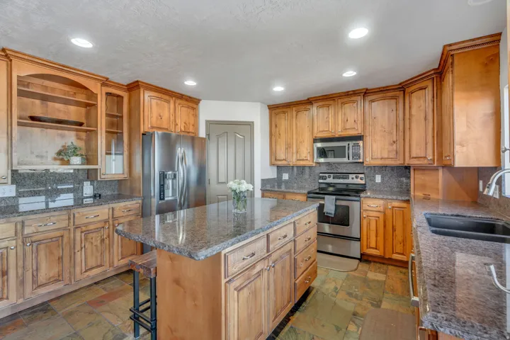 Kitchen featuring stainless steel appliances, open shelves, dark stone counters, stone tile floors, and decorative backsplash