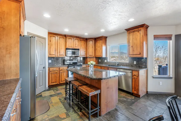 Kitchen with a kitchen bar, stainless steel appliances, wood finish cabinetry, dark stone counters, and recessed lighting