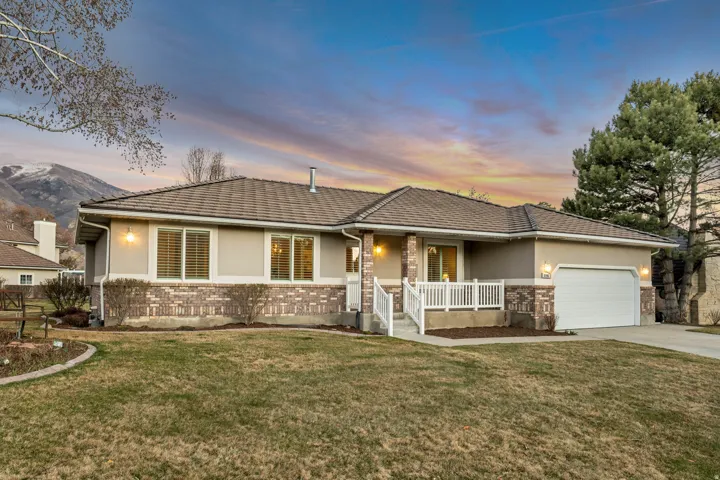 Ranch-style home with an attached garage, a lawn, stucco siding, driveway, and brick siding