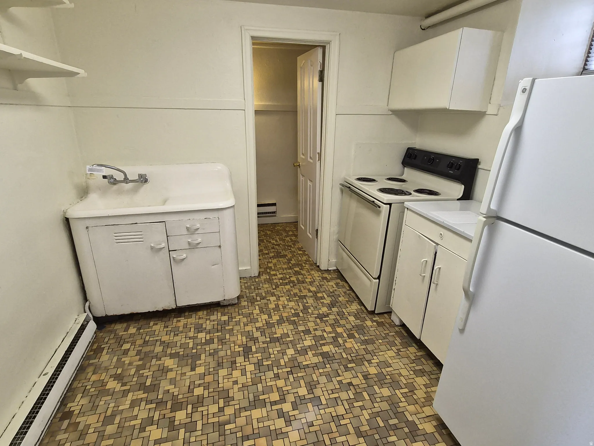 Kitchen featuring white appliances, light countertops, baseboard heating, white cabinets, and dark floors