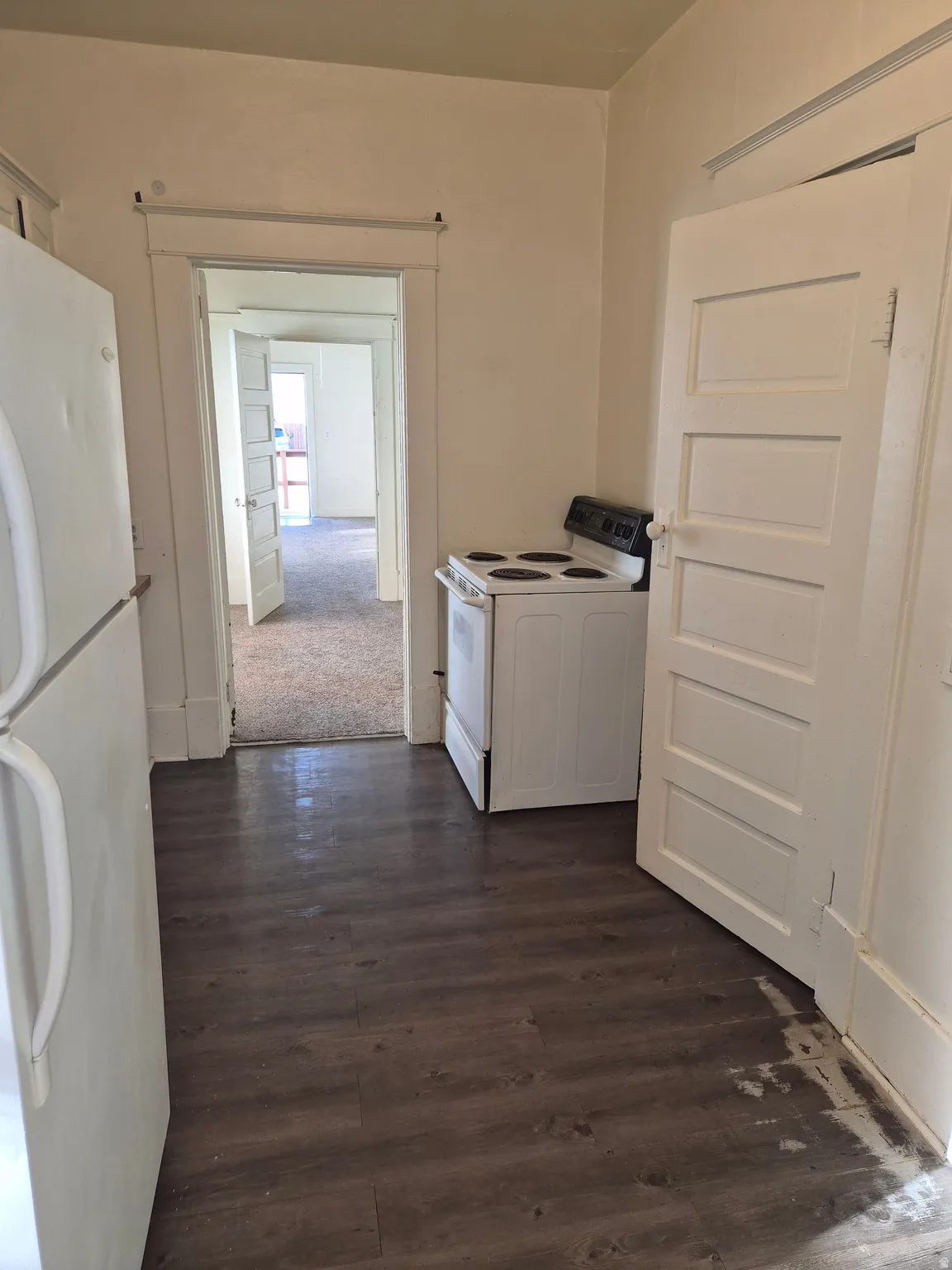 Kitchen with white appliances, washer / dryer, dark wood finished floors, white cabinetry, and dark colored carpet