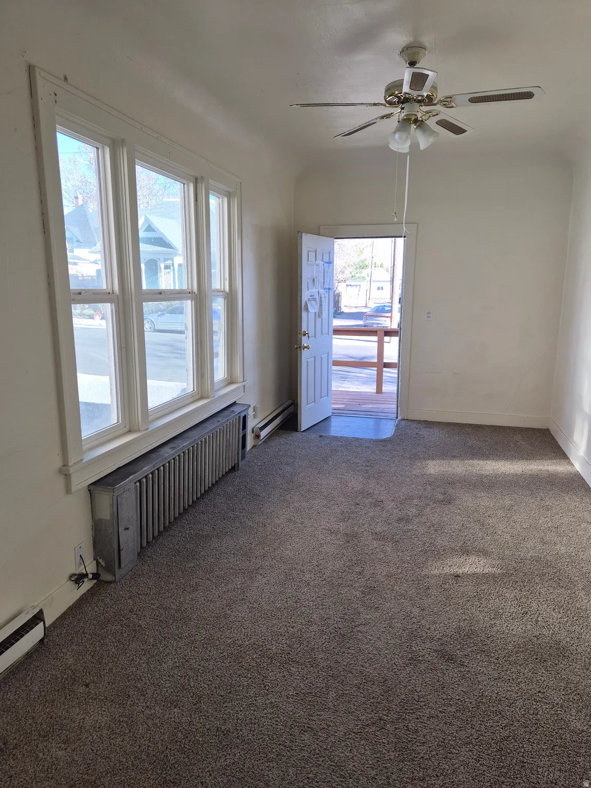Empty room featuring a ceiling fan, radiator heating unit, dark colored carpet, and baseboard heating