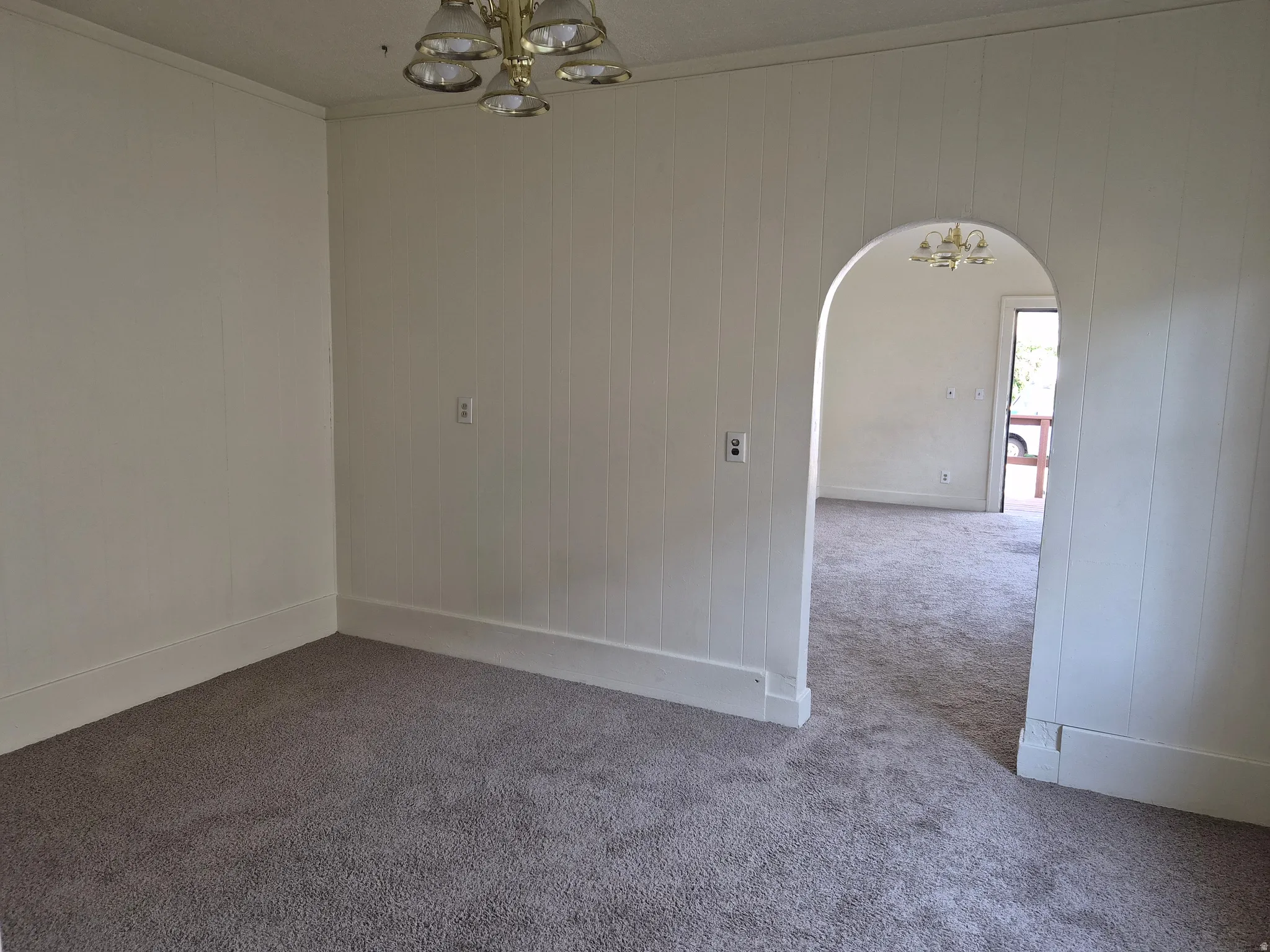 Spare room featuring a chandelier, arched walkways, ornamental molding, carpet, and wooden walls