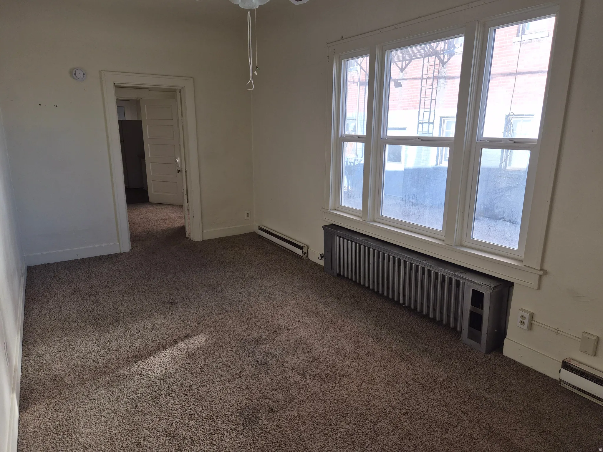 Empty room featuring carpet, radiator, and a baseboard heating unit