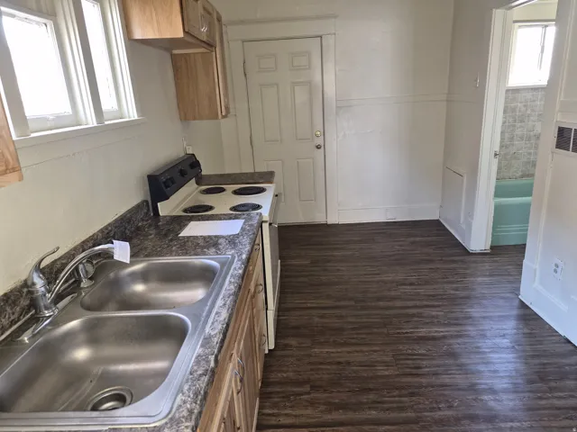 Kitchen with white range with electric stovetop, dark wood-type flooring, dark countertops, and wood finish cabinets