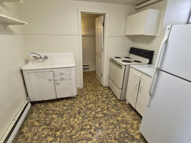 Kitchen featuring white appliances, light countertops, baseboard heating, white cabinets, and dark floors