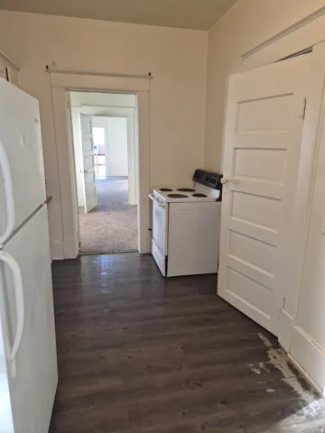 Kitchen with white appliances, washer / dryer, dark wood finished floors, white cabinetry, and dark colored carpet