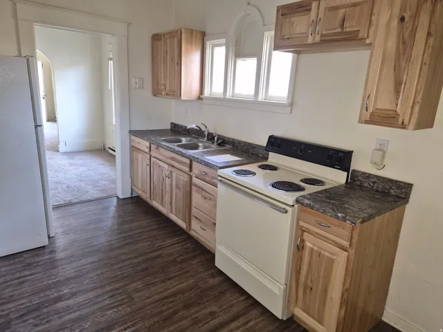 Kitchen featuring dark countertops, white appliances, arched walkways, and dark wood-style flooring