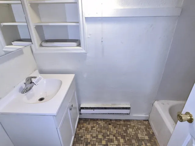 Bathroom featuring vanity, a baseboard heating unit, light flooring, and a tub