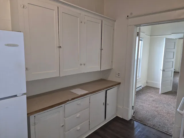 Kitchen featuring white cabinetry, freestanding refrigerator, dark wood-type flooring, and a baseboard heating unit