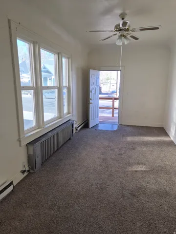 Empty room featuring a ceiling fan, radiator heating unit, dark colored carpet, and baseboard heating