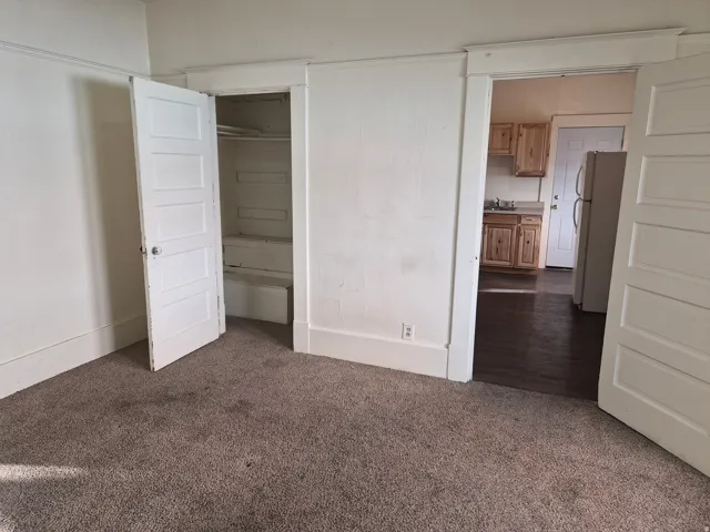 Unfurnished bedroom with dark colored carpet and freestanding refrigerator