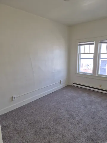 Carpeted empty room with baseboards and a baseboard radiator