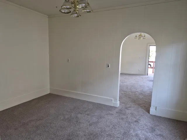Spare room featuring a chandelier, arched walkways, ornamental molding, carpet, and wooden walls