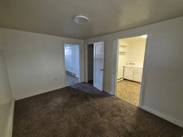 Unfurnished bedroom featuring a baseboard heating unit and dark carpet