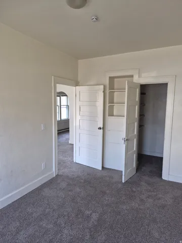 Unfurnished bedroom with a spacious closet and dark carpet