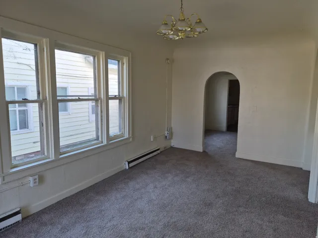 Carpeted empty room with a baseboard heating unit, arched walkways, and suspended lighting