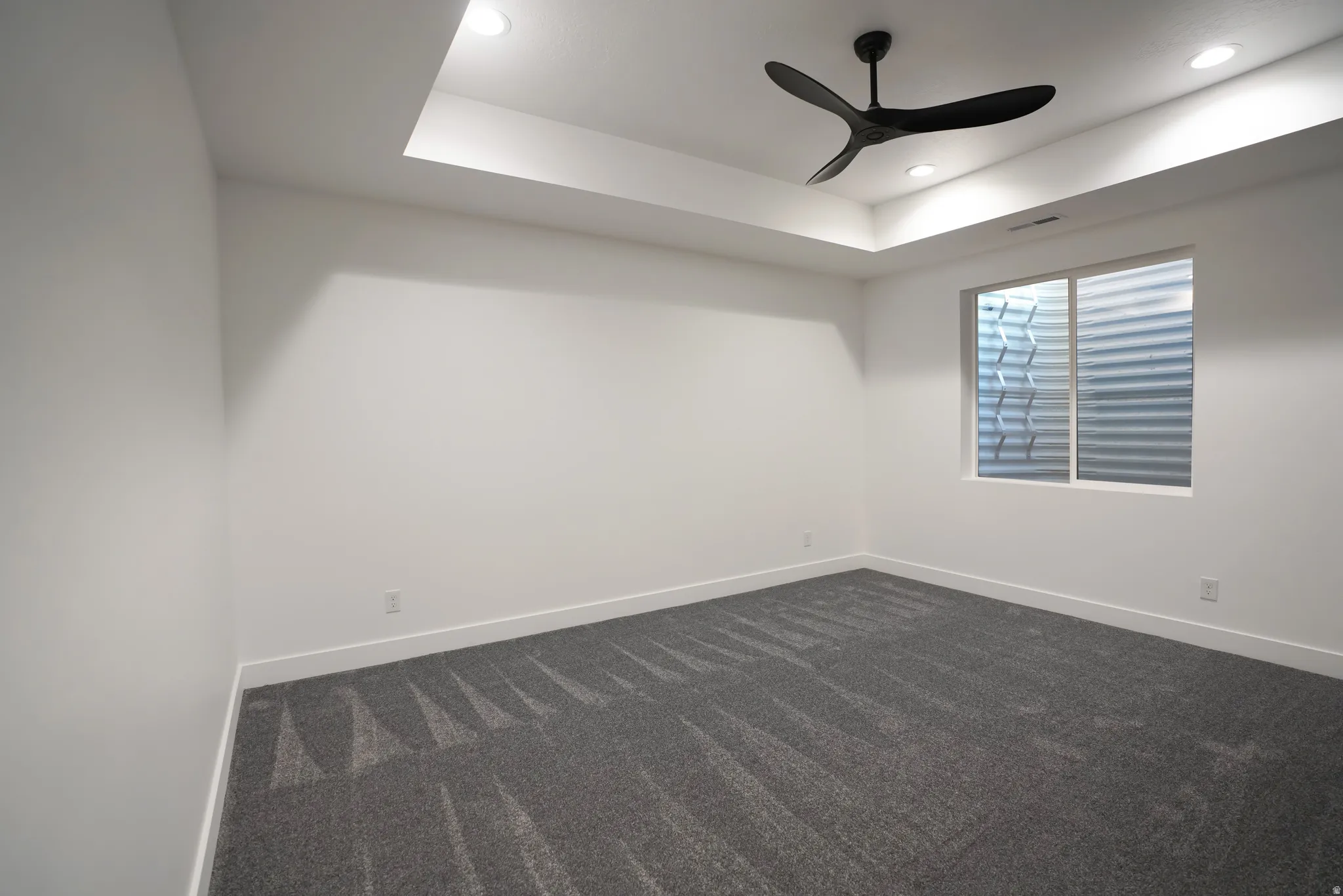 Spare room featuring dark colored carpet, a tray ceiling, recessed lighting, and a ceiling fan