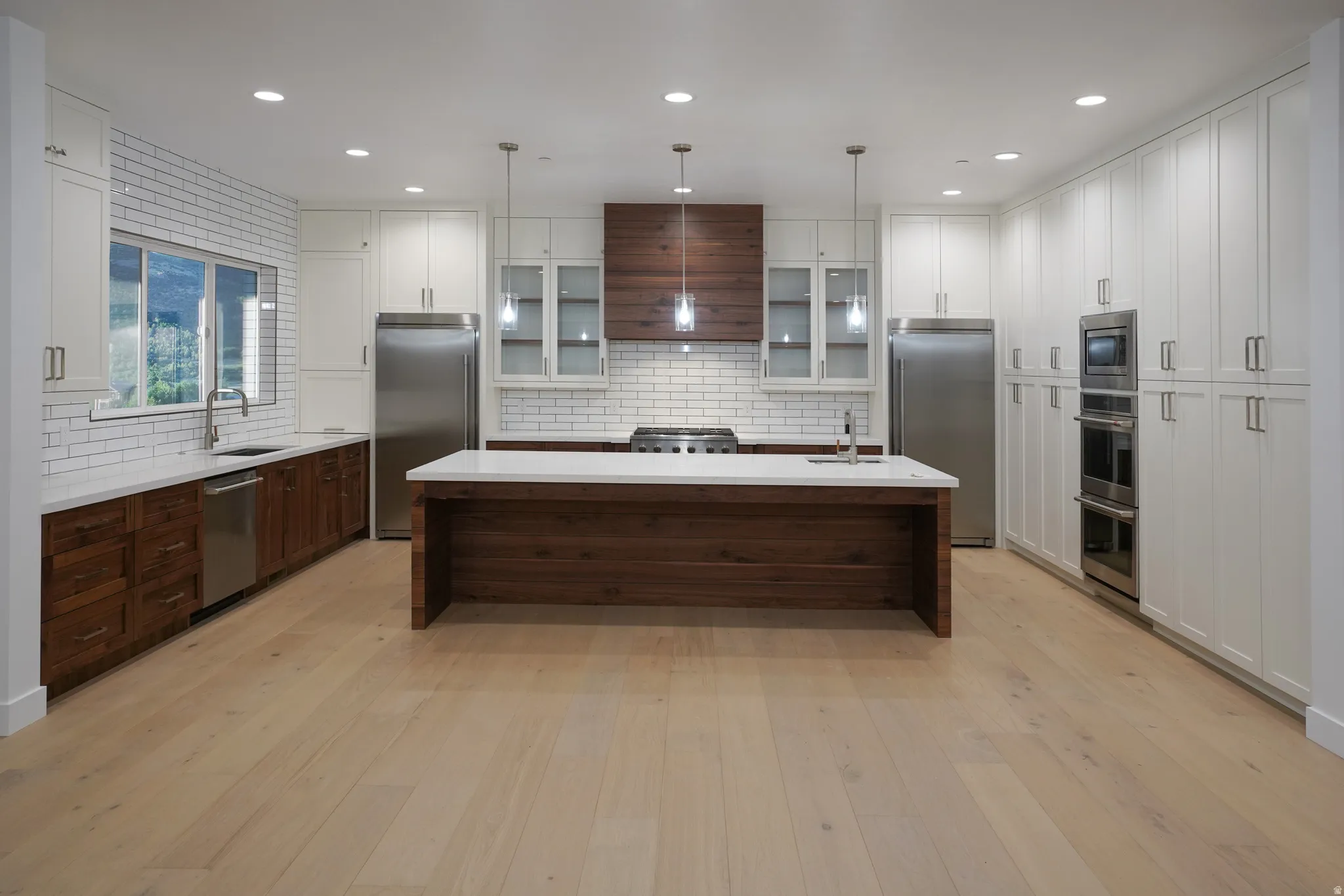 Kitchen with an island with sink, two tone color scheme, backsplash, built in appliances, and glass insert cabinets