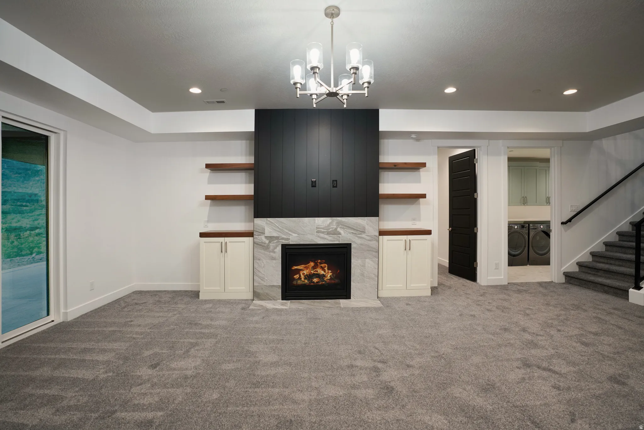 Unfurnished living room with carpet floors, a high end fireplace, washer and dryer, and suspended lighting