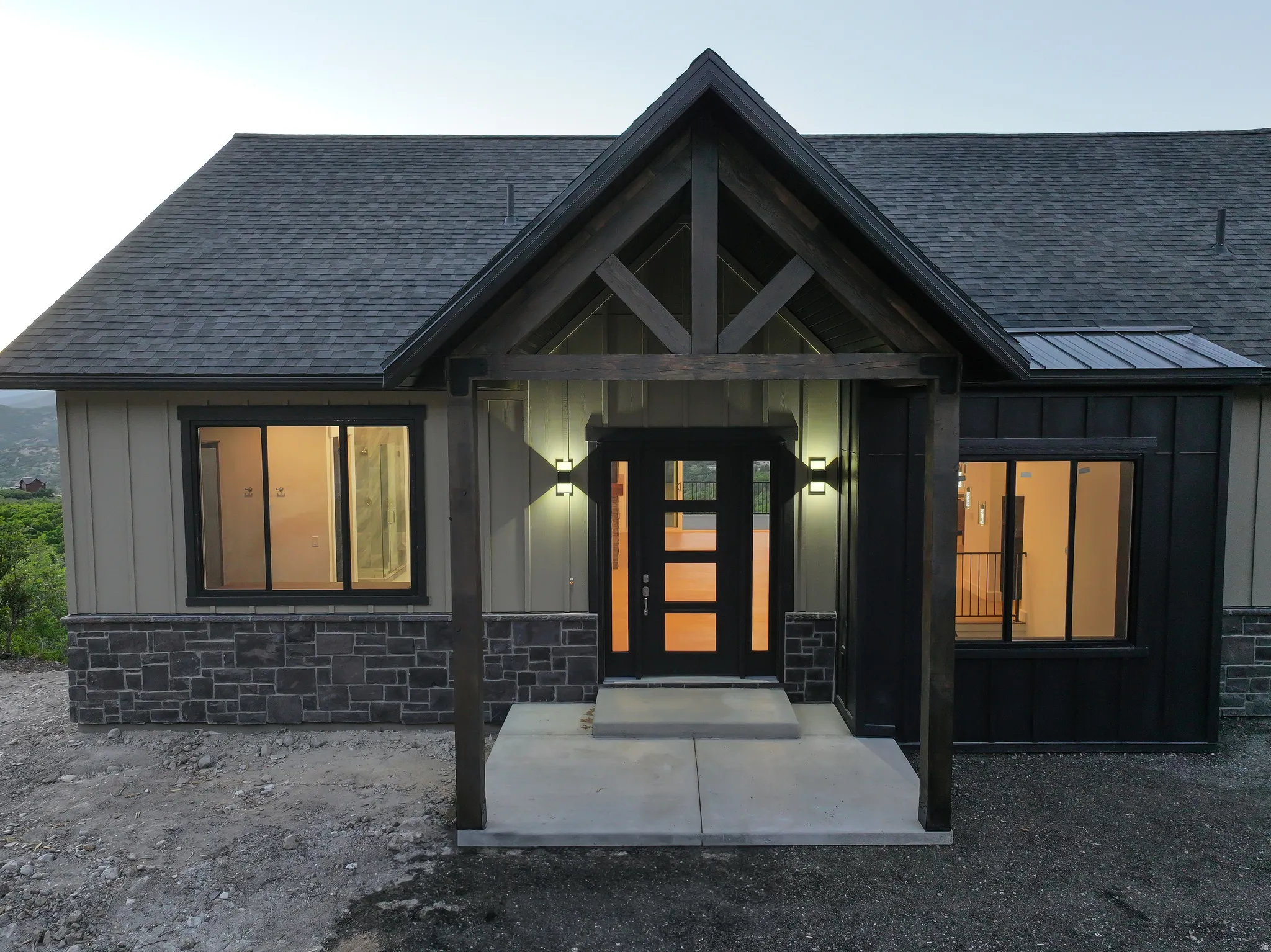 Entrance to property with board and batten siding, a shingled roof, stone siding, covered porch, and a standing seam roof