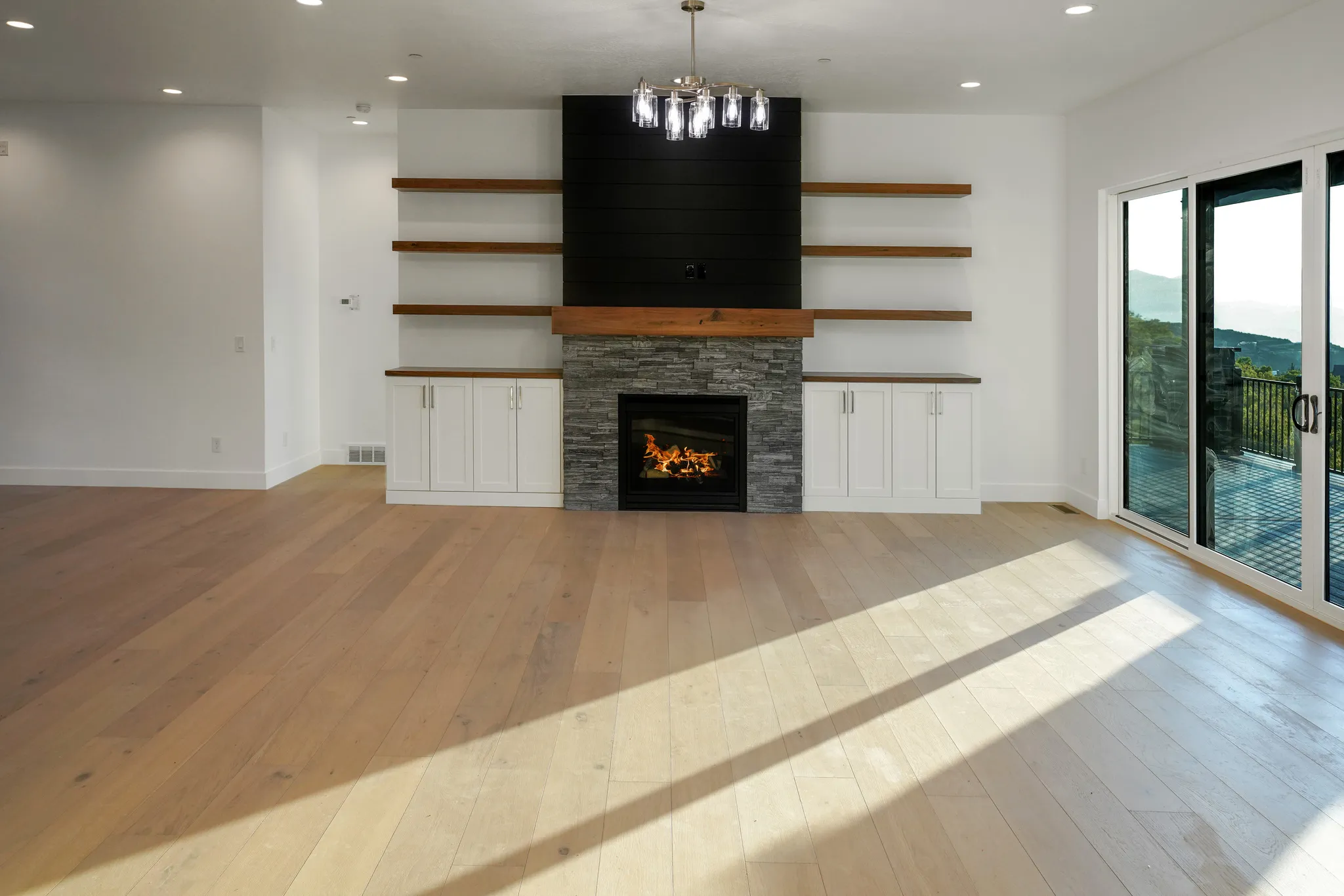 Unfurnished living room with light wood-type flooring, a stone fireplace, and suspended lighting