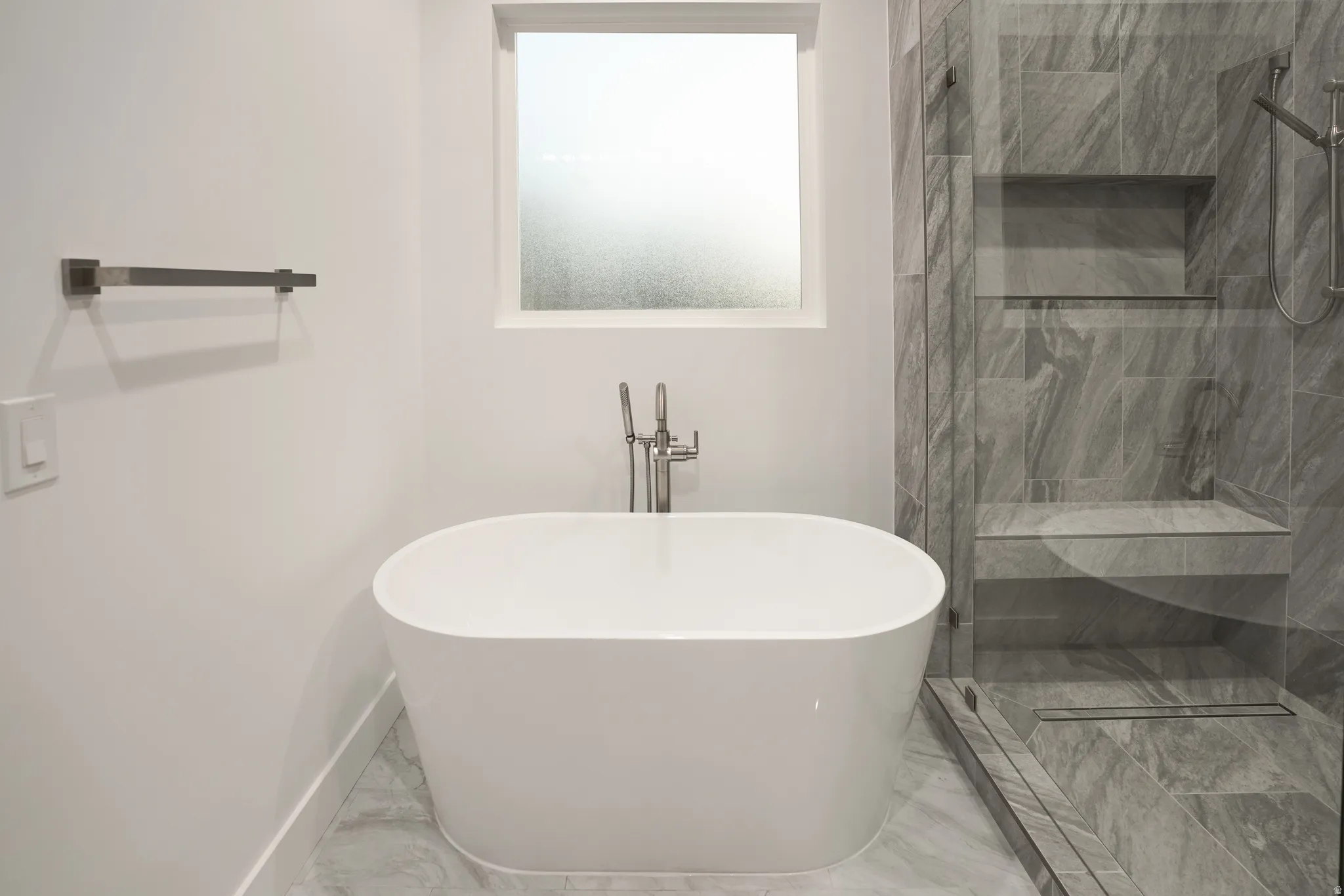 Full bathroom featuring light marble finish flooring, a freestanding bath, and walk in shower