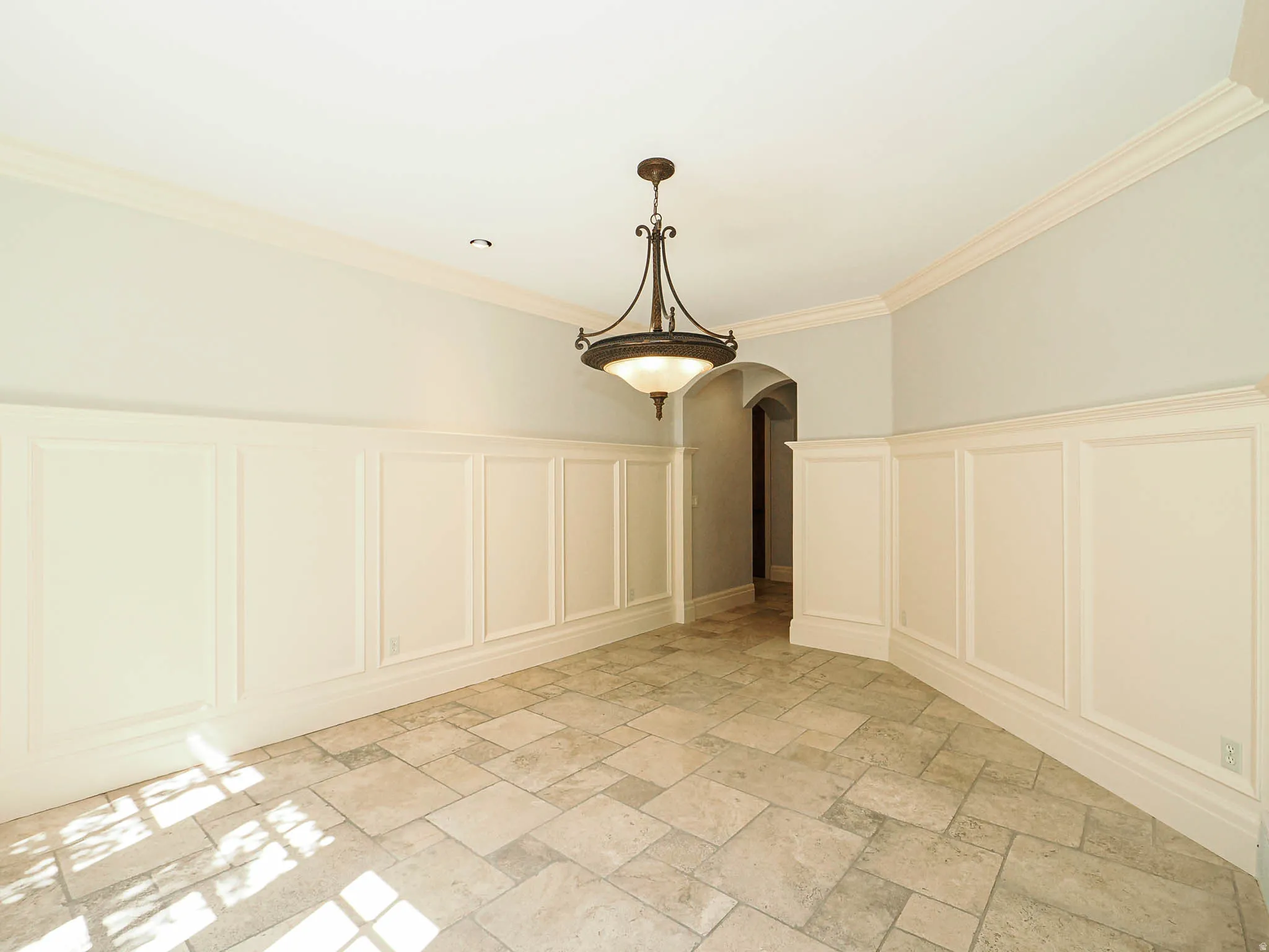 Unfurnished dining area featuring a decorative wall, a wainscoted wall, arched walkways, crown molding, and stone tile flooring