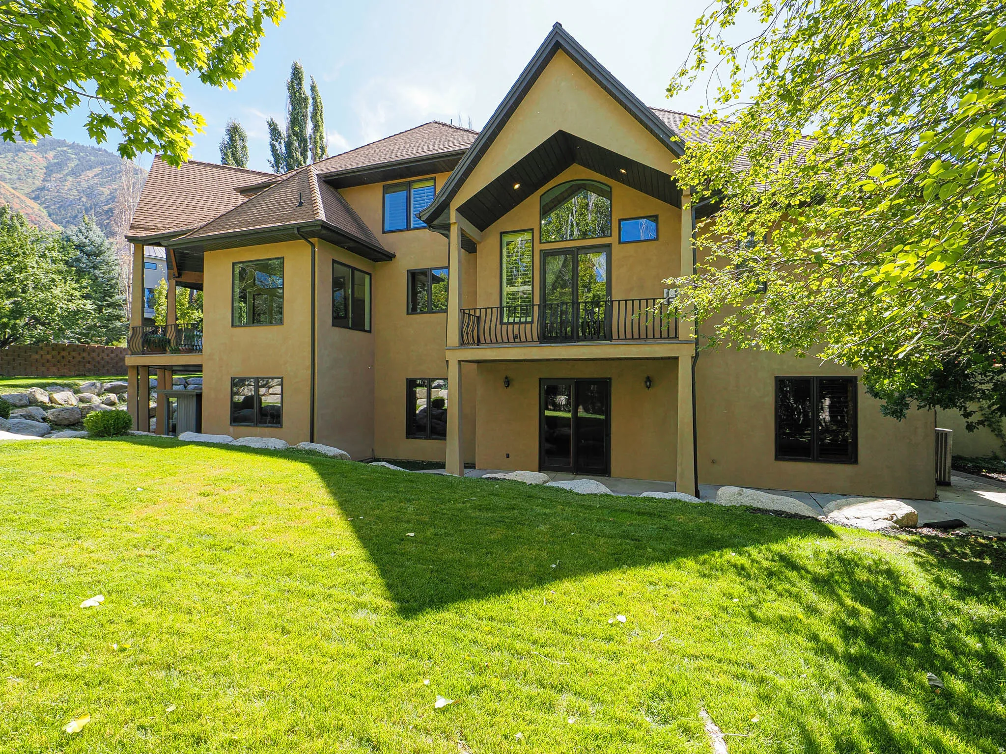 Back of house with a balcony, stucco siding, a lawn, a patio area, and roof with shingles